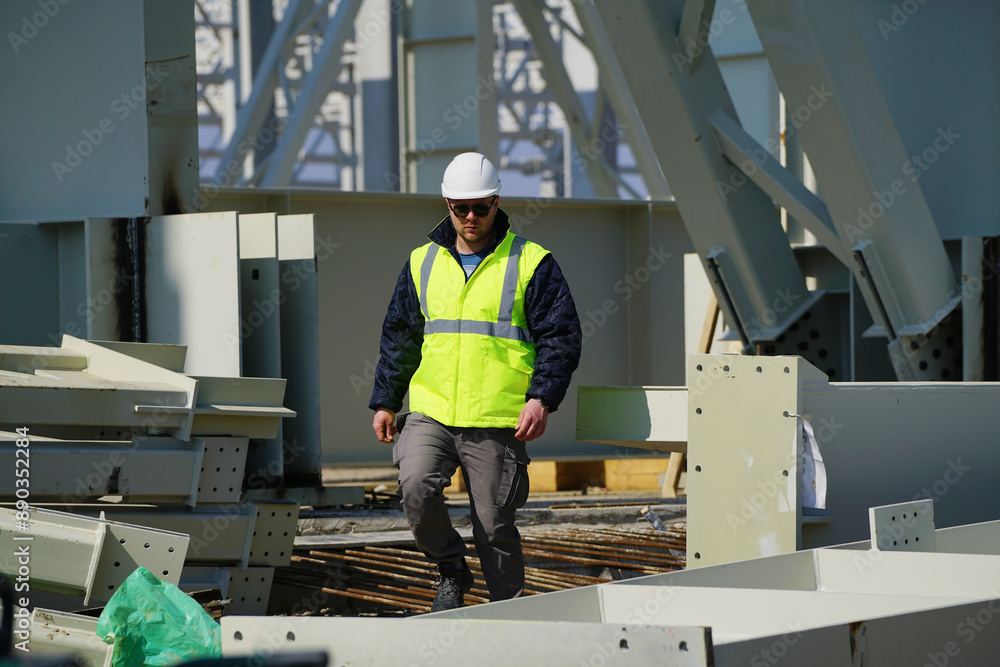 Worker Contractor Wearing Hard Hat and Safety Vests Walks on Industrial Building Construction Site. In the Background Crane, Skyscraper Concrete Worker Contractor Wearing Hard Hat and Safety Vests Walks on Industrial Building Construction Site. In the Background Crane, Skyscraper Concrete