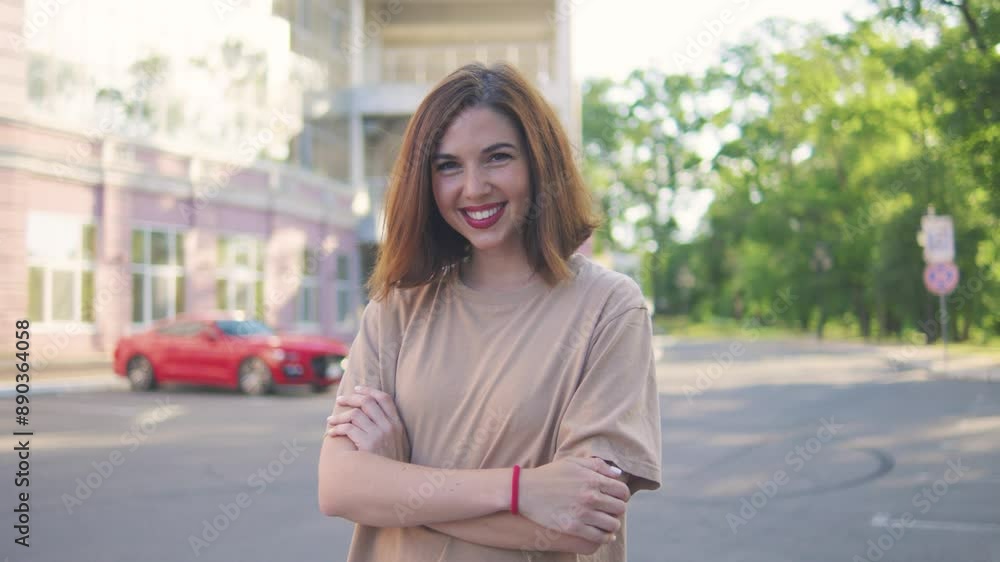 In a modern city setting under the summer sun, a brunette woman with crossed arms exudes confidence and a friendly smile, radiating a feeling of joy and positivity in her casual attire In a modern city setting under the summer sun, a brunette woman with crossed arms exudes confidence and a friendly smile, radiating a feeling of joy and positivity in her casual attire