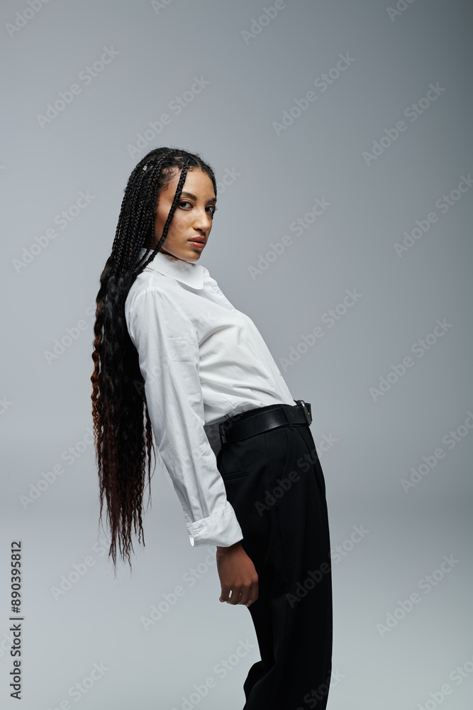 A young woman with long braids and a white shirt poses against a grey backdrop. A young woman with long braids and a white shirt poses against a grey backdrop.