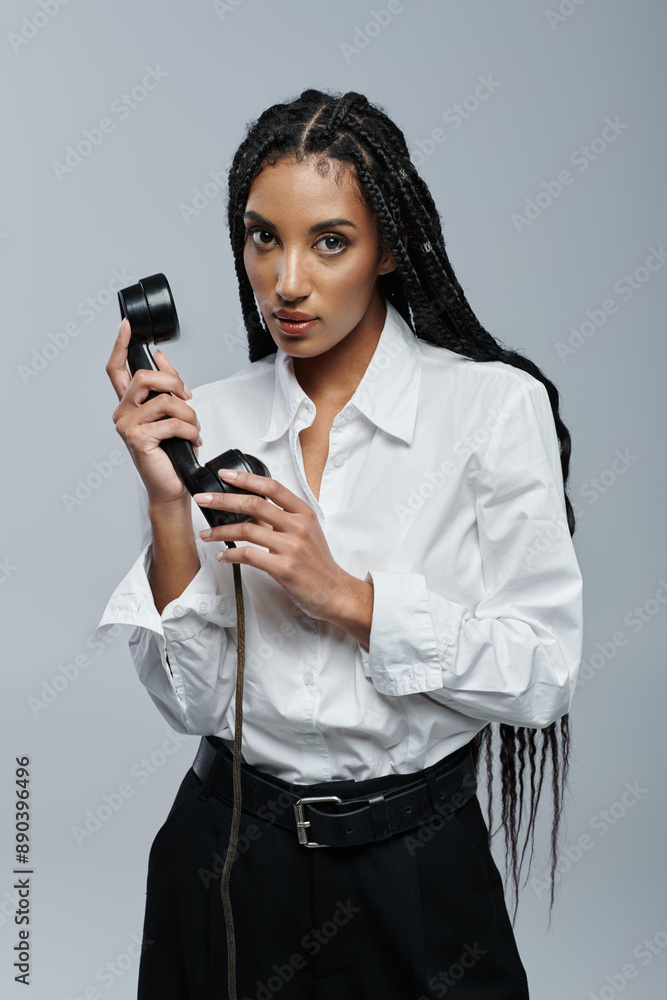 An African American woman holds an old-fashioned phone, exuding mystery as she gazes at the viewer against a grey backdrop An African American woman holds an old-fashioned phone, exuding mystery as she gazes at the viewer against a grey backdrop