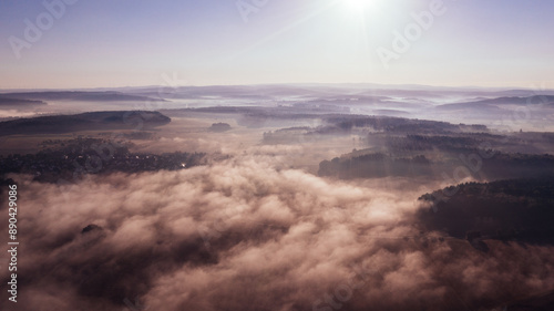 Aerial view of rolling hills covered with dense mist and a bright sun in the morning sky