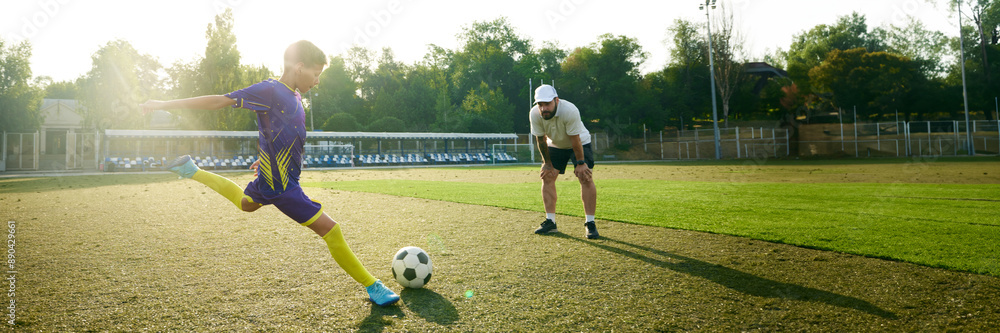 Obraz premium Banner image. Little concentrated boy in motion, running on field and hitting ball under precise look of soccer coach. Concept of sport, childhood, education, achievement, active lifestyle