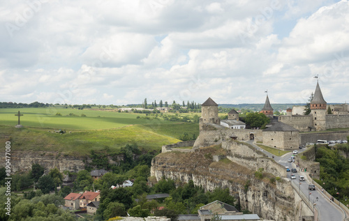 A sunny landscape of the Kamianets-Podilskyi Castle and a field. The sky is completely covered with white clouds 