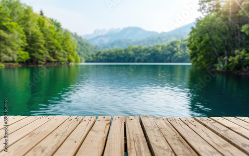 Serene lake view from a wooden pier, surrounded by lush greenery and mountains, reflecting calm waters under a clear sky. © tonstock