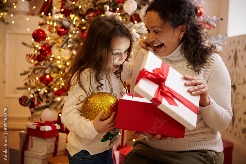 Slika na platnu Mother and daughter unwrapping Christmas gift in festive holiday setting with de