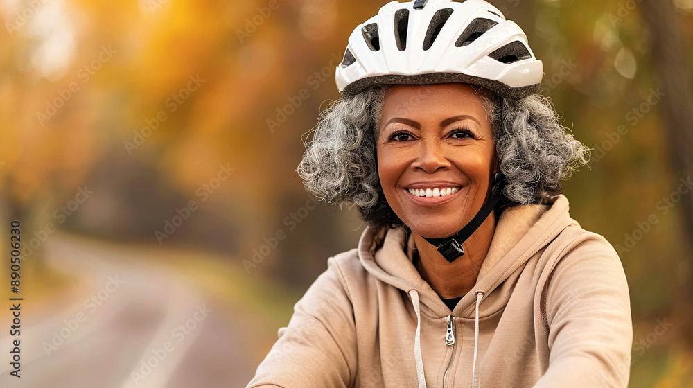 Happy smiling elderly African woman with gray curly hair in helmet and beige hoodie rides her bicycle in an autumn park. Active and healthy senior lifestyle. Copy space. Happy smiling elderly African woman with gray curly hair in helmet and beige hoodie rides her bicycle in an autumn park. Active and healthy senior lifestyle. Copy space.