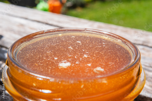 Open Honey Jar Filled with Bee Honey Standing Outside on a Wooden Table in the Garden on a Hot Sunny Summer Day Extreme Close Up photo