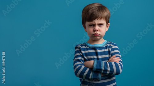 Obraz na płótnie Mad male kid, angry little boy standing with his arms crossed, and looking at the camera with upset face expression. Unhappy toddler, studio shot, annoyed and frustrated child emotion w salonie