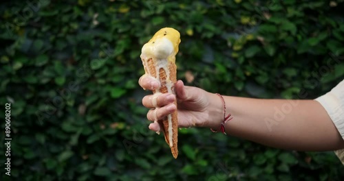A close up of a woman hand holding a waffle cone with vanilla ice cream, which melts and flows down her hand. Ice cream flows and drips onto your hand. Extreme heat. Summer background.