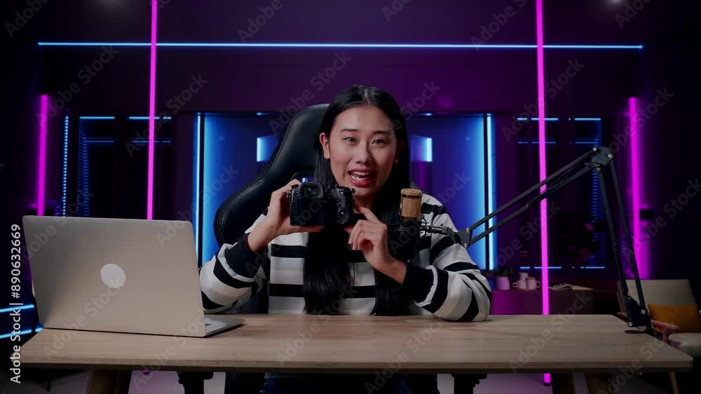 A Smiling Asian Woman With Headphone And Computer Reviewing Camera In Room Lit By Neon Lights In Retro A Smiling Asian Woman With Headphone And Computer Reviewing Camera In Room Lit By Neon Lights In Retro