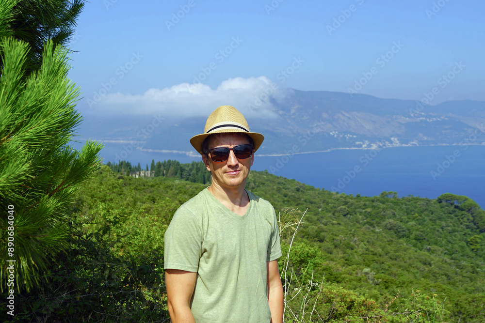 Portrait of a young smiling man relaxing in the Kotor Bay in summer. A satisfied tourist against the backdrop of the sea, forest, and coastline (viewpoint Klinci, Lustica peninsula, Montenegro). Portrait of a young smiling man relaxing in the Kotor Bay in summer. A satisfied tourist against the backdrop of the sea, forest, and coastline (viewpoint Klinci, Lustica peninsula, Montenegro).