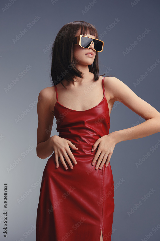 Stunning woman wearing a red dress and sunglasses strikes a pose against a neutral gray background, embodying elegance and confidence Stunning woman wearing a red dress and sunglasses strikes a pose against a neutral gray background, embodying elegance and confidence