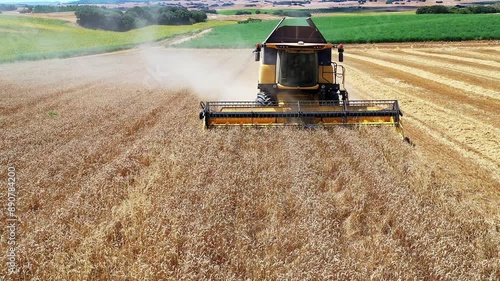 A combine harvester moves through a golden wheat field in Oteiza, Navarra, Spain, captured from the front perspective. The machine efficiently cuts through the wheat