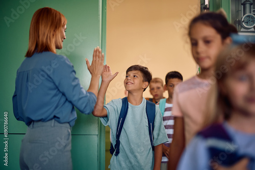 Fotografija Happy school kids greeting their teacher while entering in  classroom
