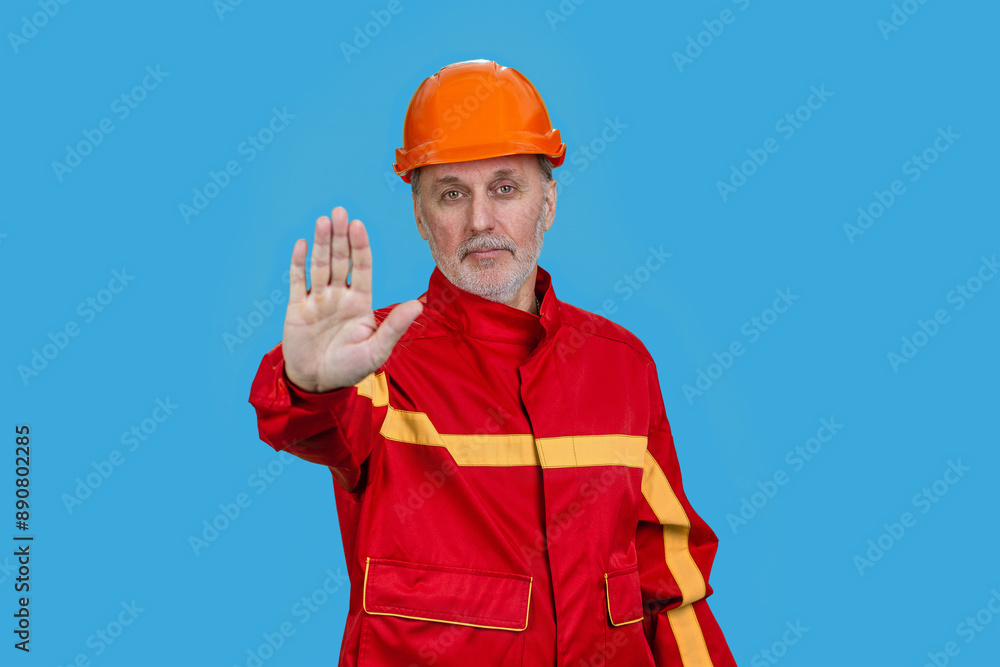 Smiling old caucasian worker shows the prohibition sign. Isolated on blue. Smiling old caucasian worker shows the prohibition sign. Isolated on blue.
