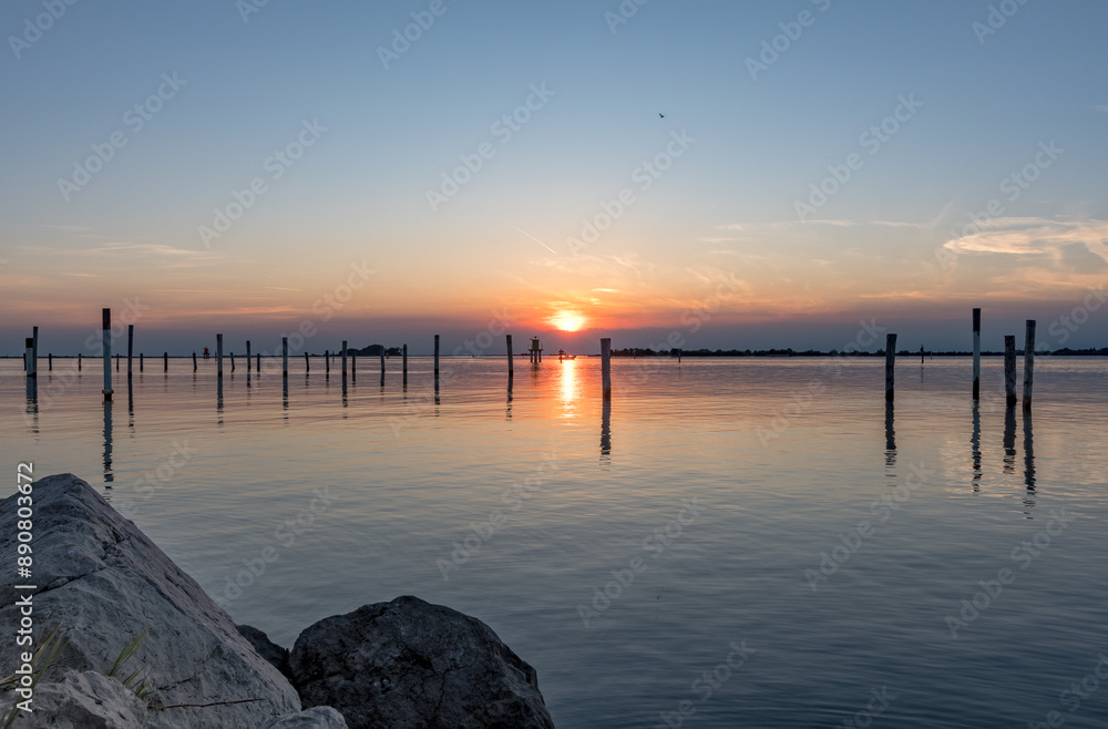Serene Sunset on the Sea in Grado: Splendid Reflections and Colors Admired from a Rocky Pier. Serene Sunset on the Sea in Grado: Splendid Reflections and Colors Admired from a Rocky Pier.