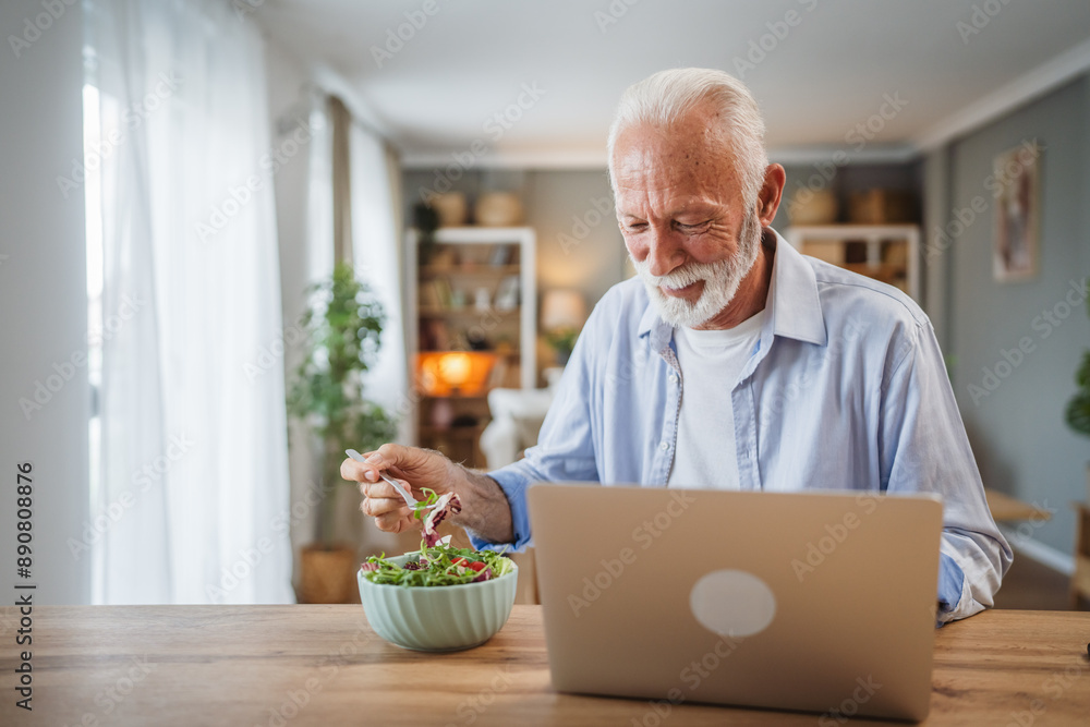 Senior caucasian man use laptop while eat salad at home Senior caucasian man use laptop while eat salad at home