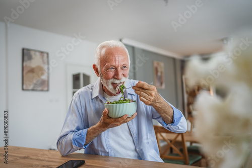 Portrait of senior man stand at home and eat salad photo