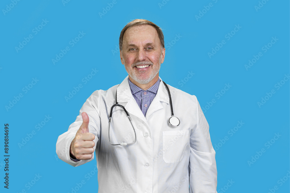 Smiling male aged senior doctor wearing stethoscope giving his thumb up. Isolated in the blue background. Smiling male aged senior doctor wearing stethoscope giving his thumb up. Isolated in the blue background.