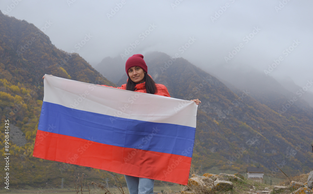Close-up of the Russian flag fluttering beautifully in the hands of a woman against the backdrop of the Caucasus Mountains on a cloudy foggy day. Russian Independence Day