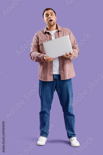 Shocked young man with laptop on violet background