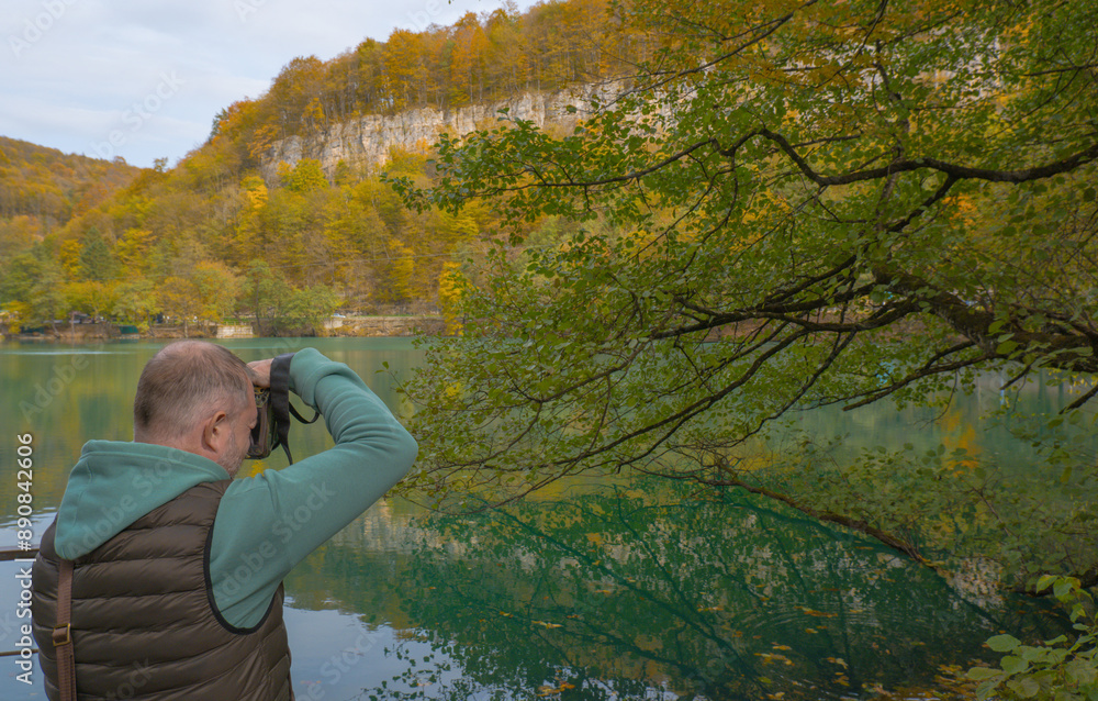 A male tourist photographs a beautiful autumn landscape with a lake in the mountains