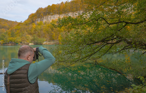 Obraz na płótnie A male tourist photographs a beautiful autumn landscape with a lake in the mountains w salonie