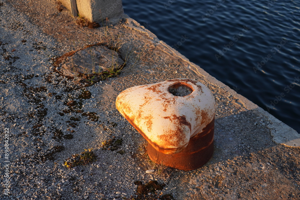 Obraz premium Close up of old rusted peach mooring bollard on the stone pier.. Navy sea water. Noblessner, Tallinn, Estonia. July 2024