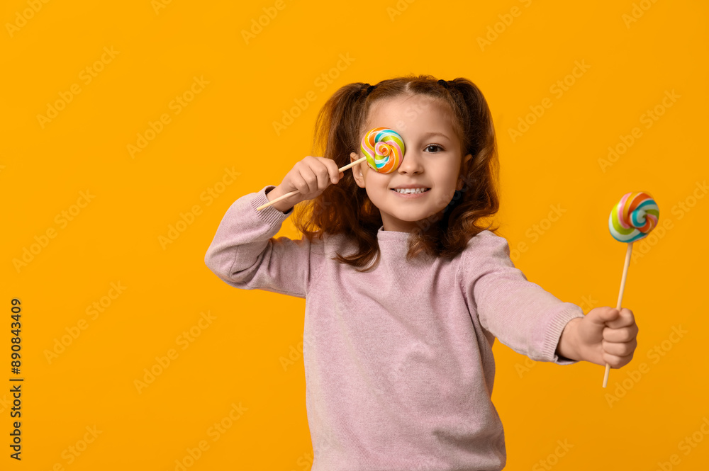 Cute little girl covering one eye with lollipop on color background Cute little girl covering one eye with lollipop on color background