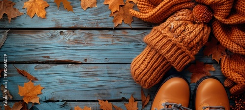 Orange Knitted Hat, Boots, and Scarf on Blue Wooden Background With Autumn Le...
