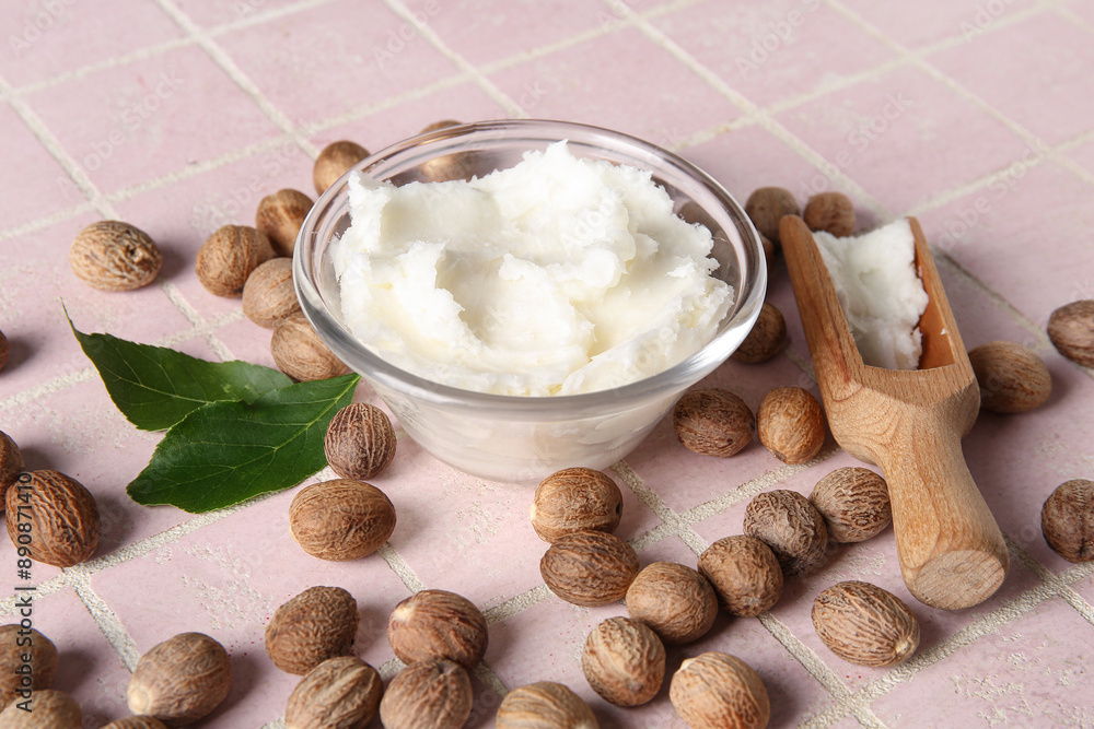 Glass bowl and scoop of shea butter with nuts on pink tile background Glass bowl and scoop of shea butter with nuts on pink tile background