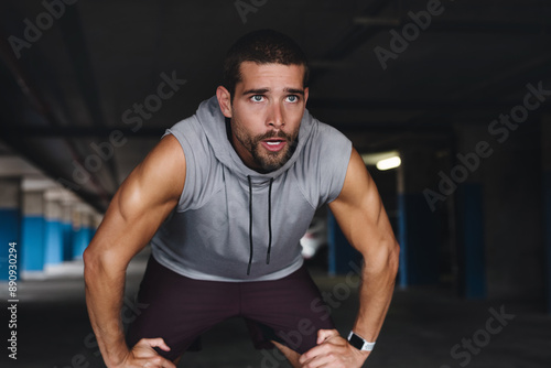 Tired, breathe and man with break in exercise for sports training, fatigue and workout recovery. Exhausted, athlete and person with rest in parking lot for fitness, challenge and run in morning photo