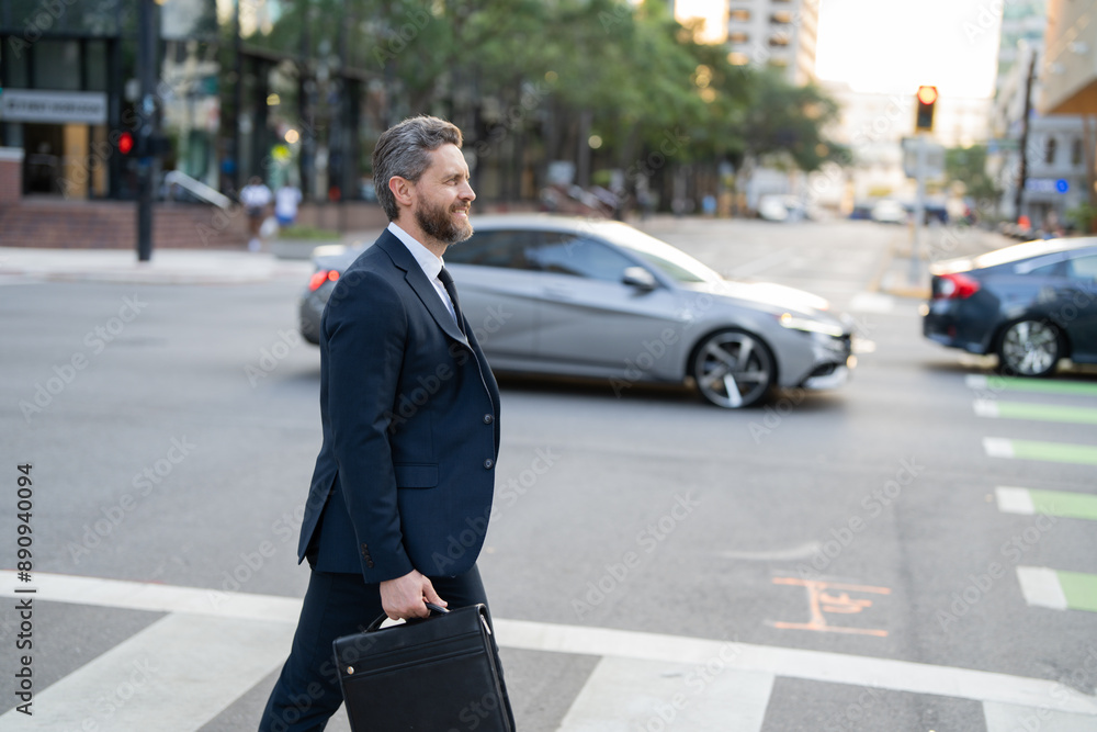 Businessman with backpack walking in city. Side view of male entrepreneur in classy suit and with takeaway drink walking along crosswalk while commuting to work in morning. businessman in the street Businessman with backpack walking in city. Side view of male entrepreneur in classy suit and with takeaway drink walking along crosswalk while commuting to work in morning. businessman in the street