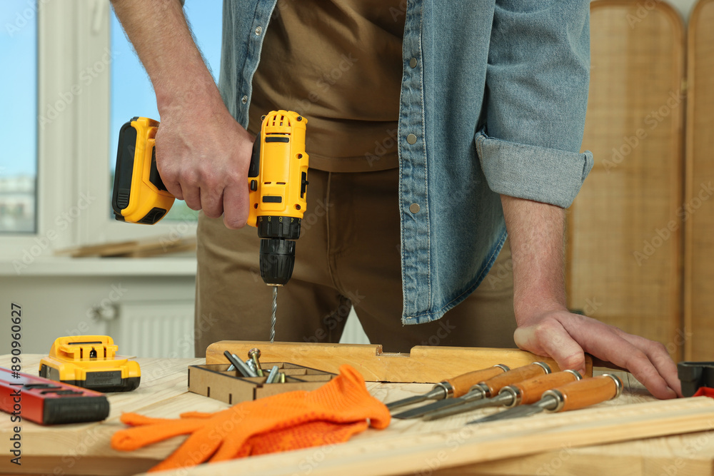 Craftsman working with drill at wooden table in workshop, closeup Craftsman working with drill at wooden table in workshop, closeup