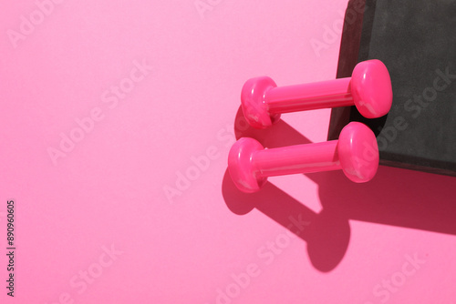 Dumbbells and yoga block on pink background, flat lay. Space for text