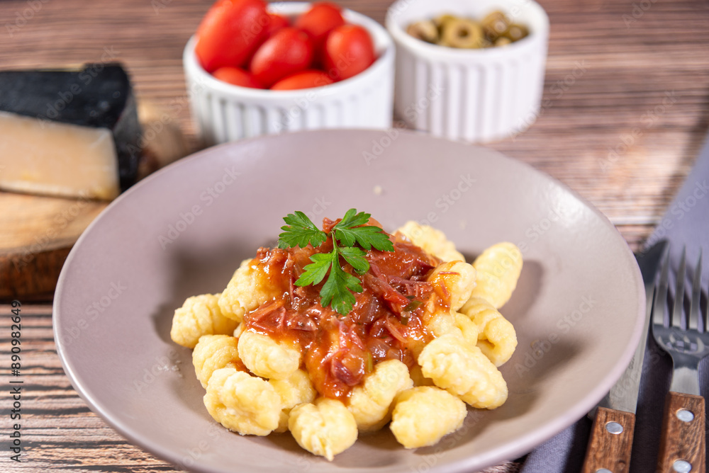 Gnocchi with parmesan cheese on the side in tomato sauce on a wooden table with preparation components around it Gnocchi with parmesan cheese on the side in tomato sauce on a wooden table with preparation components around it