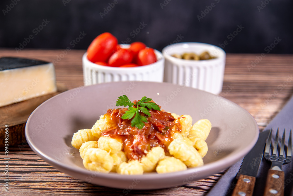 Gnocchi with grated parmesan cheese in tomato sauce on a wooden table with preparation components around it Gnocchi with grated parmesan cheese in tomato sauce on a wooden table with preparation components around it