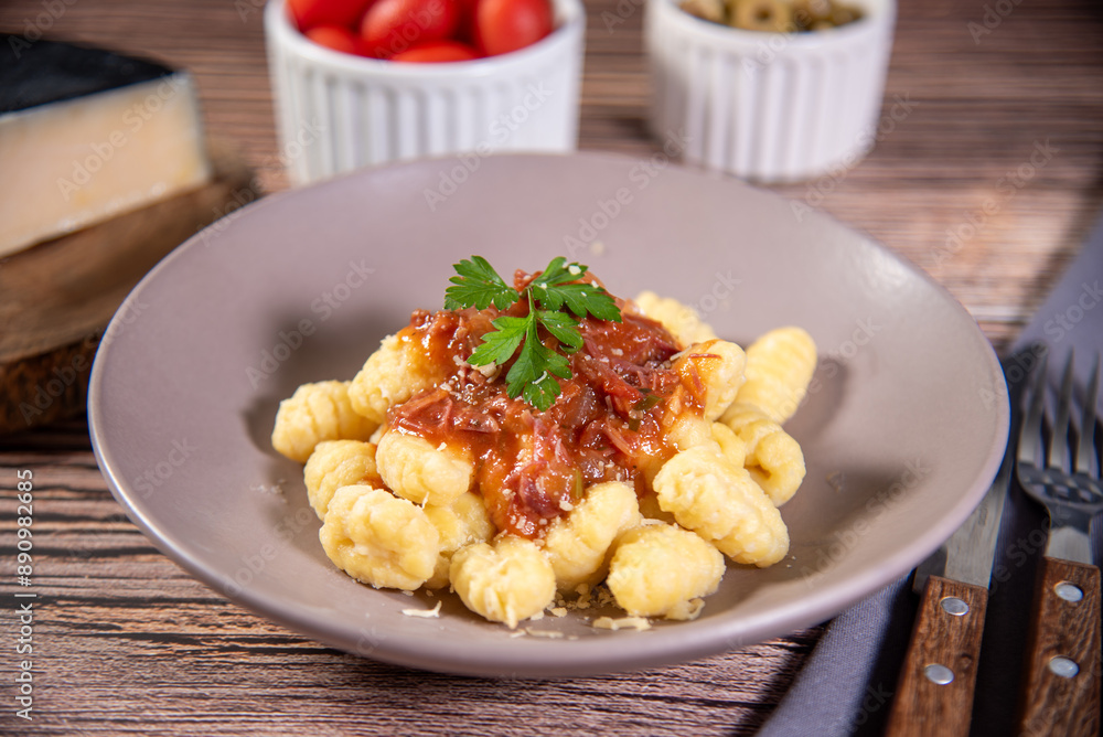 Gnocchi with grated parmesan cheese in tomato sauce on a wooden table with preparation components around it Gnocchi with grated parmesan cheese in tomato sauce on a wooden table with preparation components around it