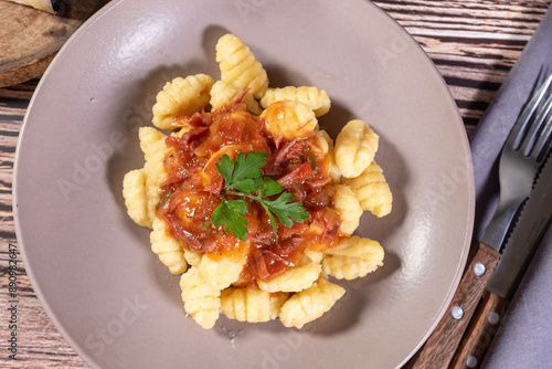 Gnocchi with parmesan cheese on the side in tomato sauce on a wooden table with preparation components around it