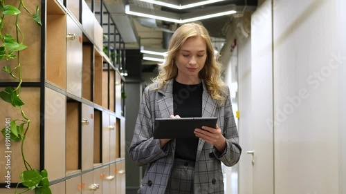 Businesswoman walking in corridor using an iPad. Woman with a smile walks behind the lockers in a modern office.