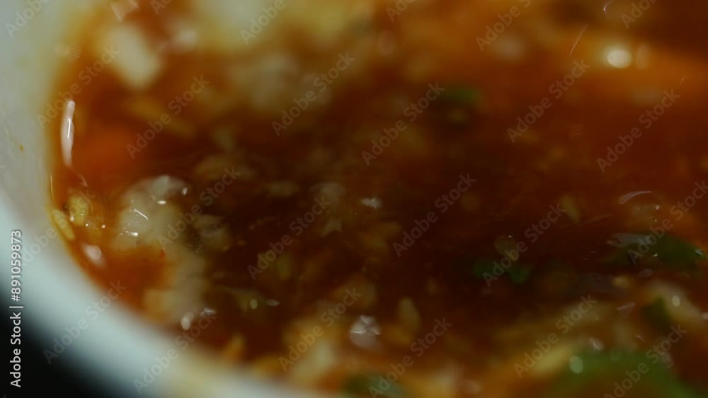 A bowl of red soup with green herbs and spices. The soup is full of flavor and looks delicious A bowl of red soup with green herbs and spices. The soup is full of flavor and looks delicious