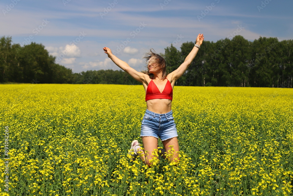 An adult happy woman in a red top and denim shorts jumps and makes a wheel element in a yellow rapeseed field. Motion blur effect. An adult happy woman in a red top and denim shorts jumps and makes a wheel element in a yellow rapeseed field. Motion blur effect.