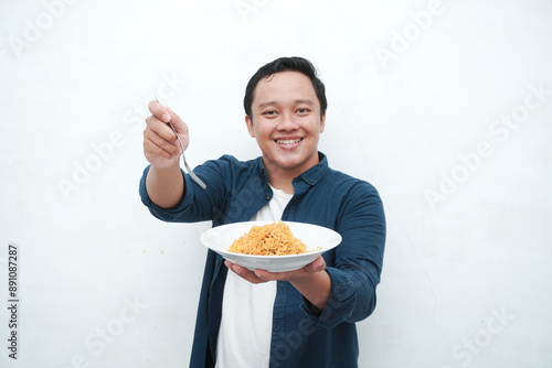 A portrait of happy Asian man wearing a blue shirt excited to eat a plate of fried noodles. Young man smiling and holding a plate of noodle. Isolated with a white background.