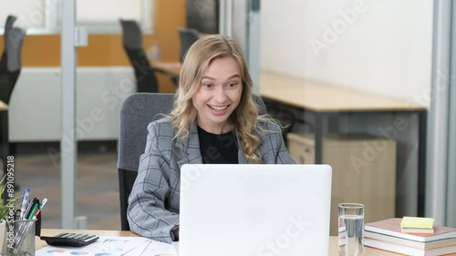 Close up of a businesswoman working on her laptop. Woman rejoicing and smiling from unbelievable good news she seeing on laptop screen and raising her hands. Modern office with tidy desk.