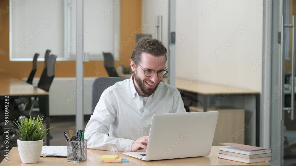 Businessman working on his laptop. Man rejoicing from unbelievable good news he seeing on laptop screen and raising his hands. Modern office with tidy desk. Businessman working on his laptop. Man rejoicing from unbelievable good news he seeing on laptop screen and raising his hands. Modern office with tidy desk.