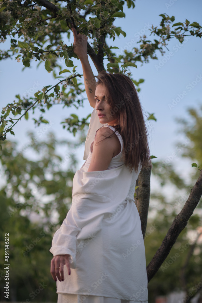 A person in white garments stretches with arms up, standing near a tree. The photo highlights the peaceful and contemplative moments found in nature. A person in white garments stretches with arms up, standing near a tree. The photo highlights the peaceful and contemplative moments found in nature.