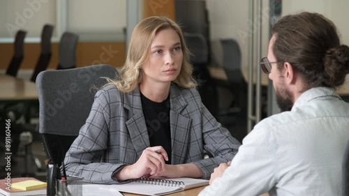 Two business professional having a serious discussion. A woman listen and take notes in front of her workmate. Office workers having a one-on-one meeting in a modern office.