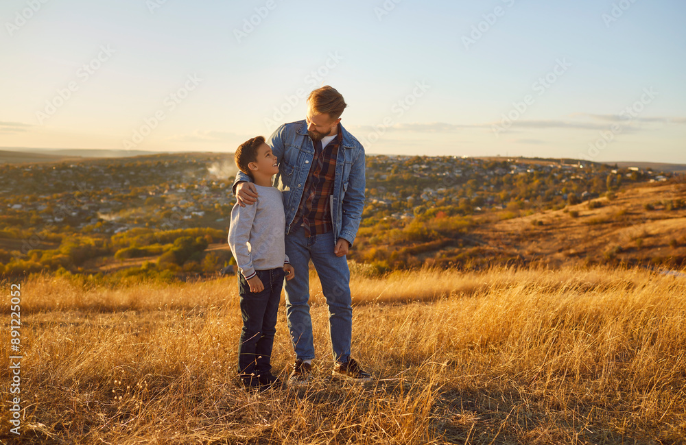 Father and son stand amidst golden yellow field at sunset. Scene depicts picturesque moment shared by father and son evoking warmth of family bonds amidst beauty of nature's embrace Father days. Father and son stand amidst golden yellow field at sunset. Scene depicts picturesque moment shared by father and son evoking warmth of family bonds amidst beauty of nature's embrace Father days.