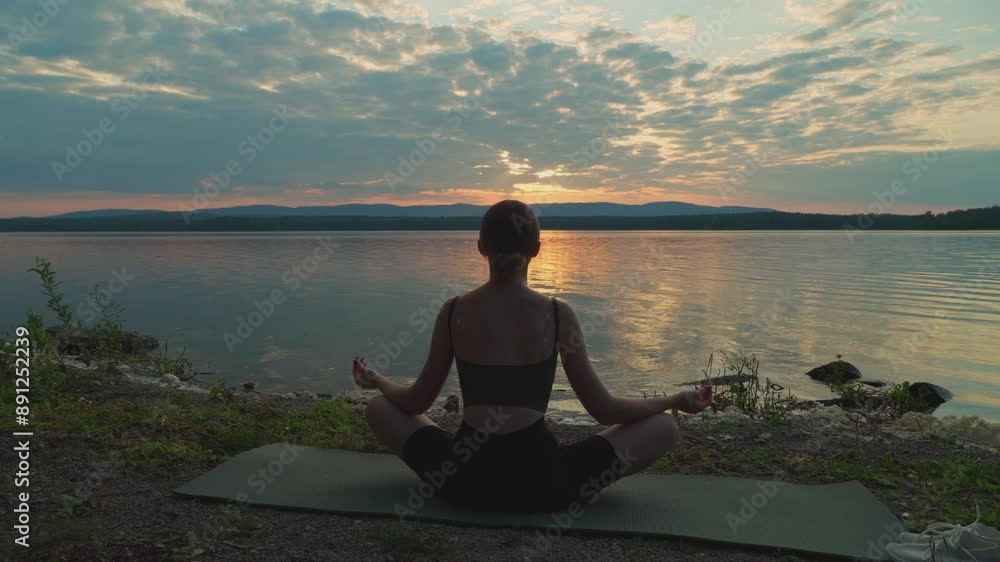 A young girl does yoga and fitness on the shore of the lake at sunset. The harmony of human privacy with nature. Sports training in nature. A young girl does yoga and fitness on the shore of the lake at sunset. The harmony of human privacy with nature. Sports training in nature.