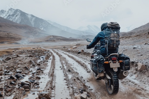 A biker is seen riding through rough, muddy terrain in a remote mountain area, carrying essential gear, highlighting the spirit of adventure and solitude.